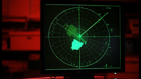 A green radar screen in a control room lit up with red light.