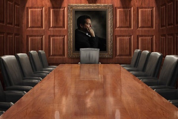 Empty board room table with black executive chairs and portrait of a man on wood paneled walls