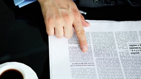 Hand pointing to line in newspaper with coffee