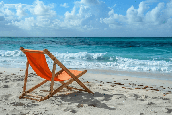 A wooden beach chair with orange canvas sitting on a beach while ocean waves roll in