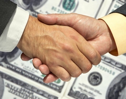 Two businessmen shaking hands over a background of one hundred dollar bills
