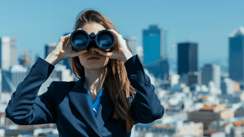Businesswoman using binoculars with a city skyline in the background