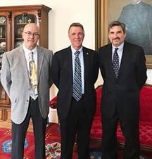 Three confident businessmen of the Vermont Captive standing shoulder to shoulder in front of wooden cabinet and painting