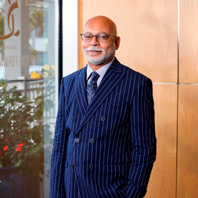 Craig Swan in a navy pinstripe suit, white shirt, and navy paisely tie by a window with red flowers outside