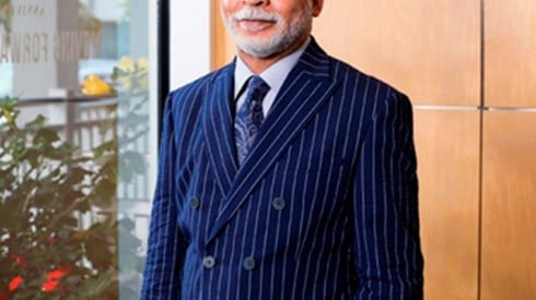Craig Swan in a navy pinstripe suit, white shirt, and navy paisely tie by a window with red flowers outside
