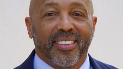 Headshot of John Talley in a navy blue suit and green tie