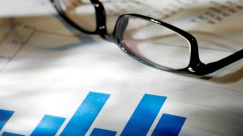 Documents with blue bar graph and financial statements with a pair of black reading glasses on top