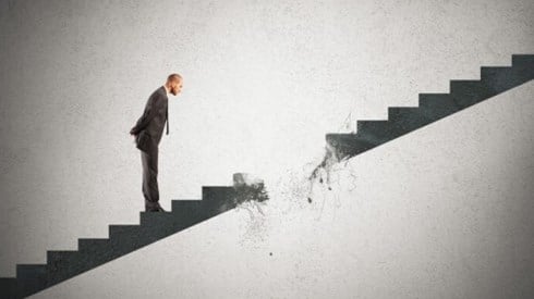 A businessman on stairs looking at a hole that is breaking in the staircase