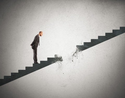 A businessman on stairs looking at a hole that is breaking in the staircase