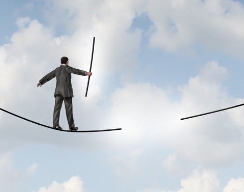 Businessman on a tightrope walking toward a missing piece in the middle of the tightrope with cloudy skies in the background