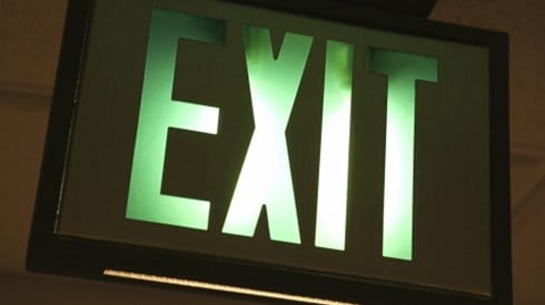 A green and white lit up EXIT sign mounted in a black frame on a ceiling