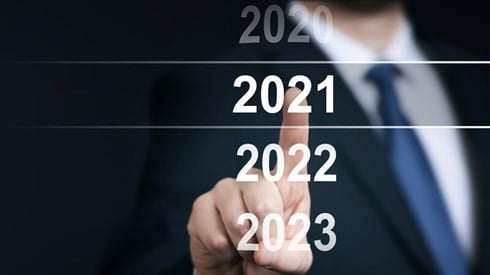 Businessman in coat and tie points at 2021 in a vertical row of number 2020-2023 where 2020 is faded out