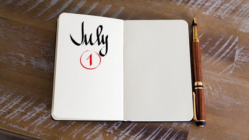 Open notepad with July 1 circled in red on left side and a blank page on right with a pen on a desk