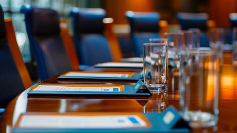 Conference table with clipboards and an empty glass in front of each blue chair
