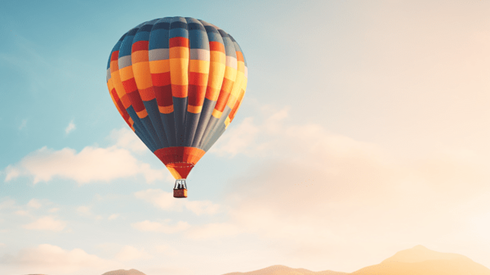 Colorful Hot Air Balloon Floats Above Mountaintops Against a Muted Partly Cloudy Sky 