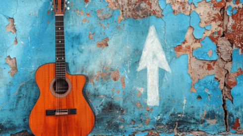 Acoustic guitar leaning against a wall with blue peeling paint and a white chalk arrow pointing up drawn on the wall