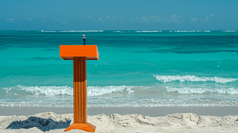 Wooden speaker podium with a microphone sitting on a beach with ocean waves rolling in