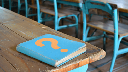 Children's primer with an orange question mark on its front cover sitiing on an old school desk