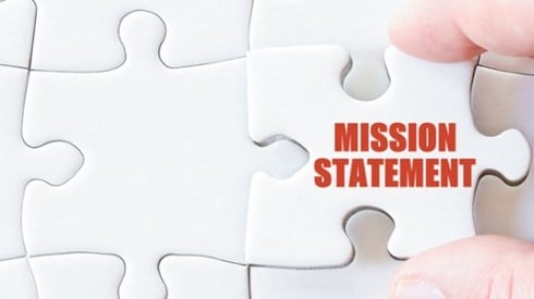 Two fingers are inserting the last piece of a puzzle that has written in red MISSION STATEMENT.