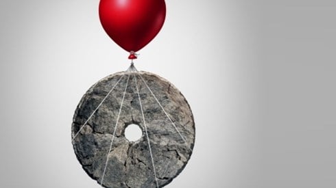 Red helium balloon attached to and lifting an ancient millstone