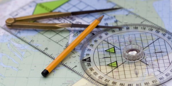 Navigational course plotting tools with compass and pencil laying on top of a map