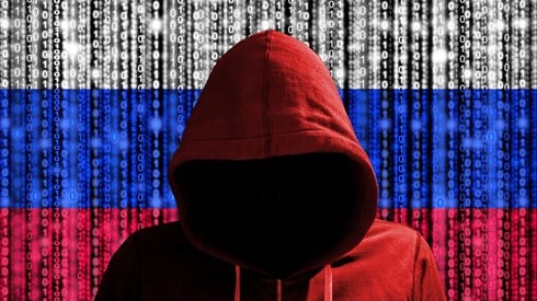 Menacing hacker dressed in a red hoodie standing in front of the Russian Federation flag with computer code on it