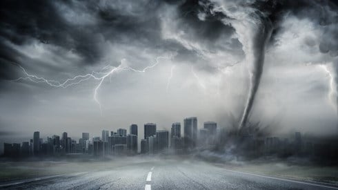 A road leading into a city with a large storm and a tornado touching down