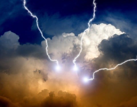 Blue sky with white and orange storm clouds emitting three white lightning bolts 