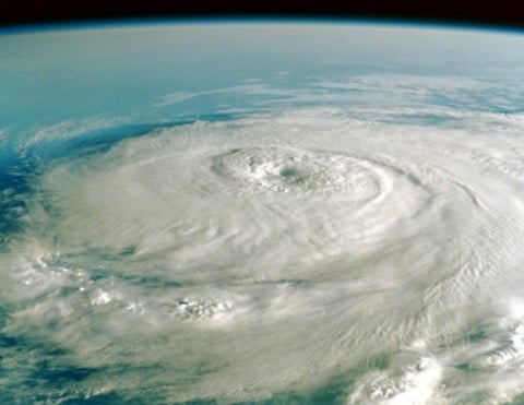 An aerial view looking down on swirling white hurricane clouds and storm with blue ocean below