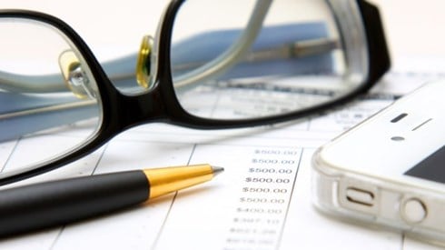 Financial statement under review with eyeglasses, black and gold pen, and smartphone on top