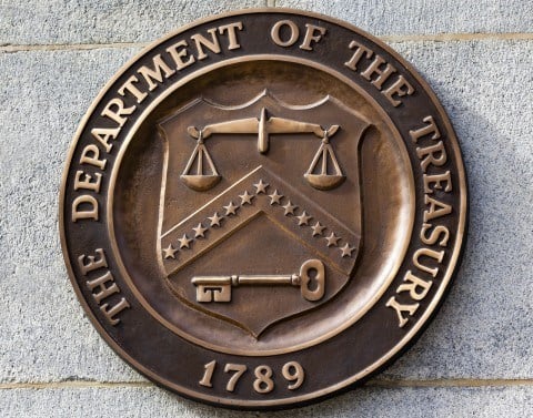 Metal sign mounted on a concrete block building showing THE DEPARTMENT OF THE TREASURY 1789 seal 