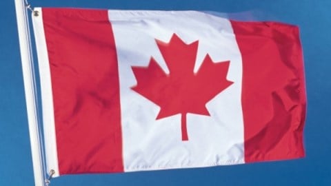 The flag of Canada waving on a white flagpole against a blue sky