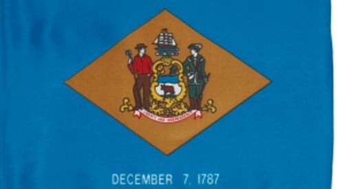 The Delaware flag with a gold color diamond in the middle of light blue material with white December 7, 1787 at bottom