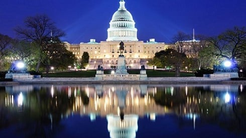 Night view of Capitol Building with reflection showing in water in front of it and spotlights shining on it