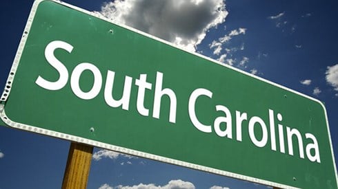 Road sign reading South Carolina against a blue sky with clouds