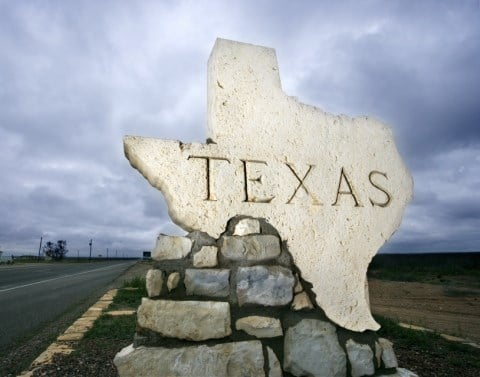 A pile of rocks mounded on the side of a road with the top rock in the shape of and word Texas in the middle welcoming incoming visitors.