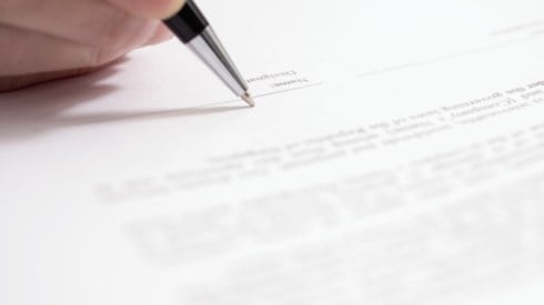 A hand holding a black pen and getting ready to sign on a signature line of a legal document