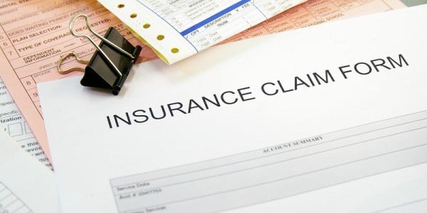 Insurance claim forms on white, yellow, and pink paper with binder black clip