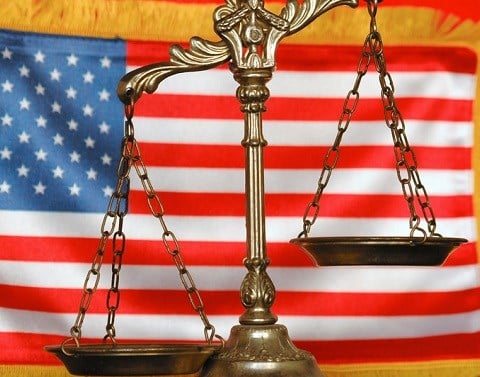 Golden scales of justice in front of an American flag with yellow fringe
