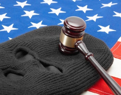 Lying on an American flag is a grey ski mask with a gavel lying on the forehead part of the mask.