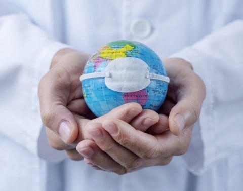 Cupped hands holding a small globe with a medical mask on it