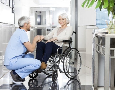 Older woman in wheelchair being greeted by a kneeling male nurse