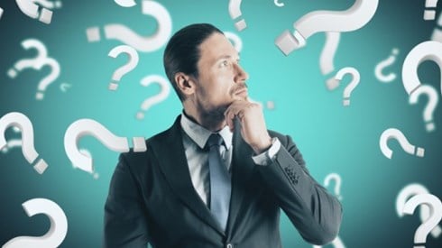 Businessman pondering surrounded by question marks