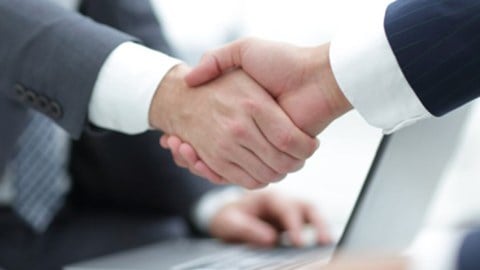 Two business people shake hands over a laptop
