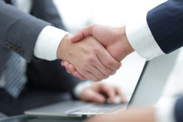 Two business people shake hands over a laptop