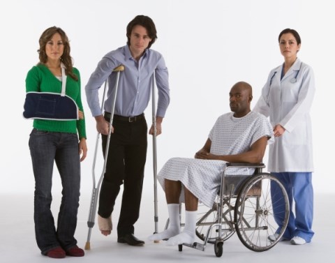 A woman with her arm in a sling, a man on crutches with a cast on his foot, and man in a wheelchair being pushed by a nurse