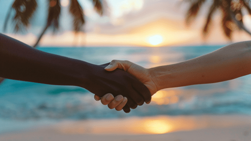 Two people shaking hands in front of a beach at sunrise