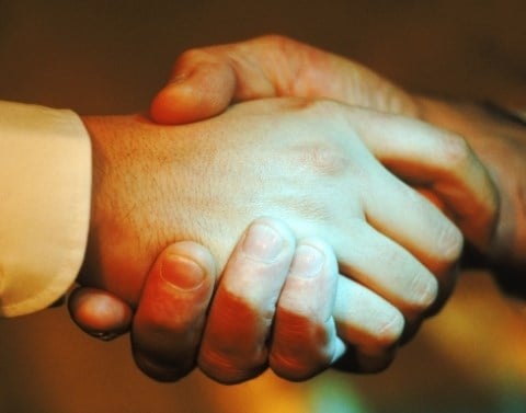 Men shaking hands with only the hands and a white dress shirt cuff visible and a blurred background