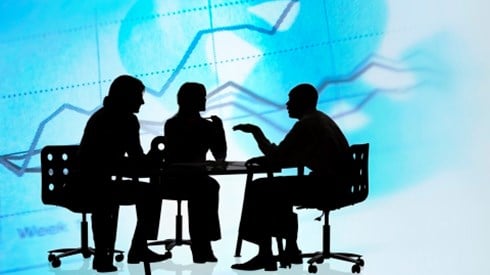 Silhouette of several people outlined in black in a meeting around a table with charts and graphs in the background