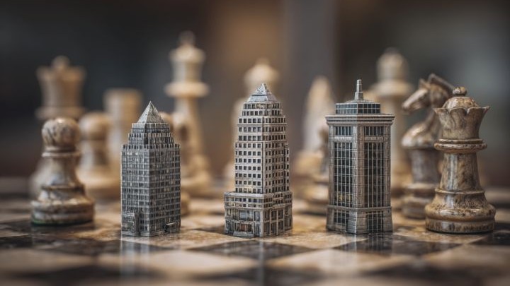 commercial buildings as chess pieces on a chess board surrounded by regular chess pieces